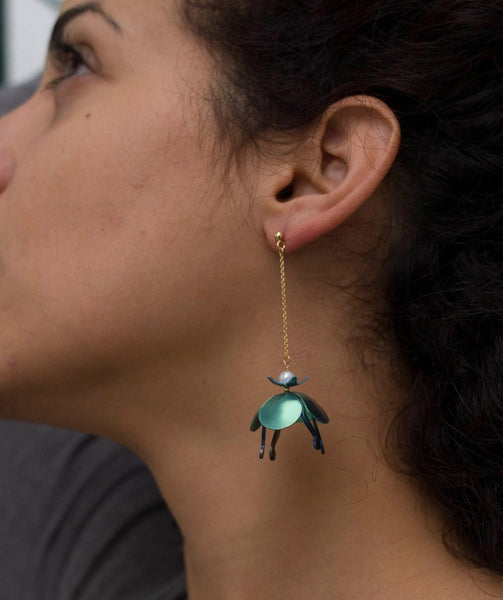 Model wearing long earrings with golden chain and colorful titanium water lilies in blue, red and green.